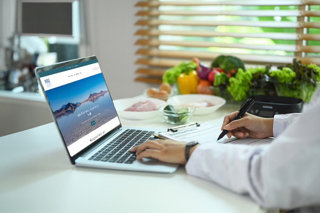 Person using a laptop with a scenic website on a kitchen counter with produce.